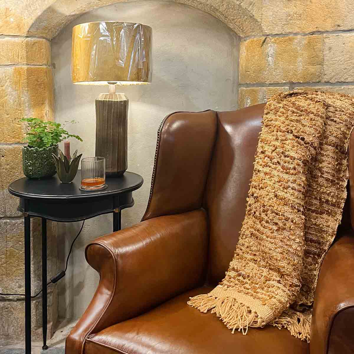 Cazar Throw in brown draped over a leather armchair, styled with a side table and warm lighting for a cosy setting.