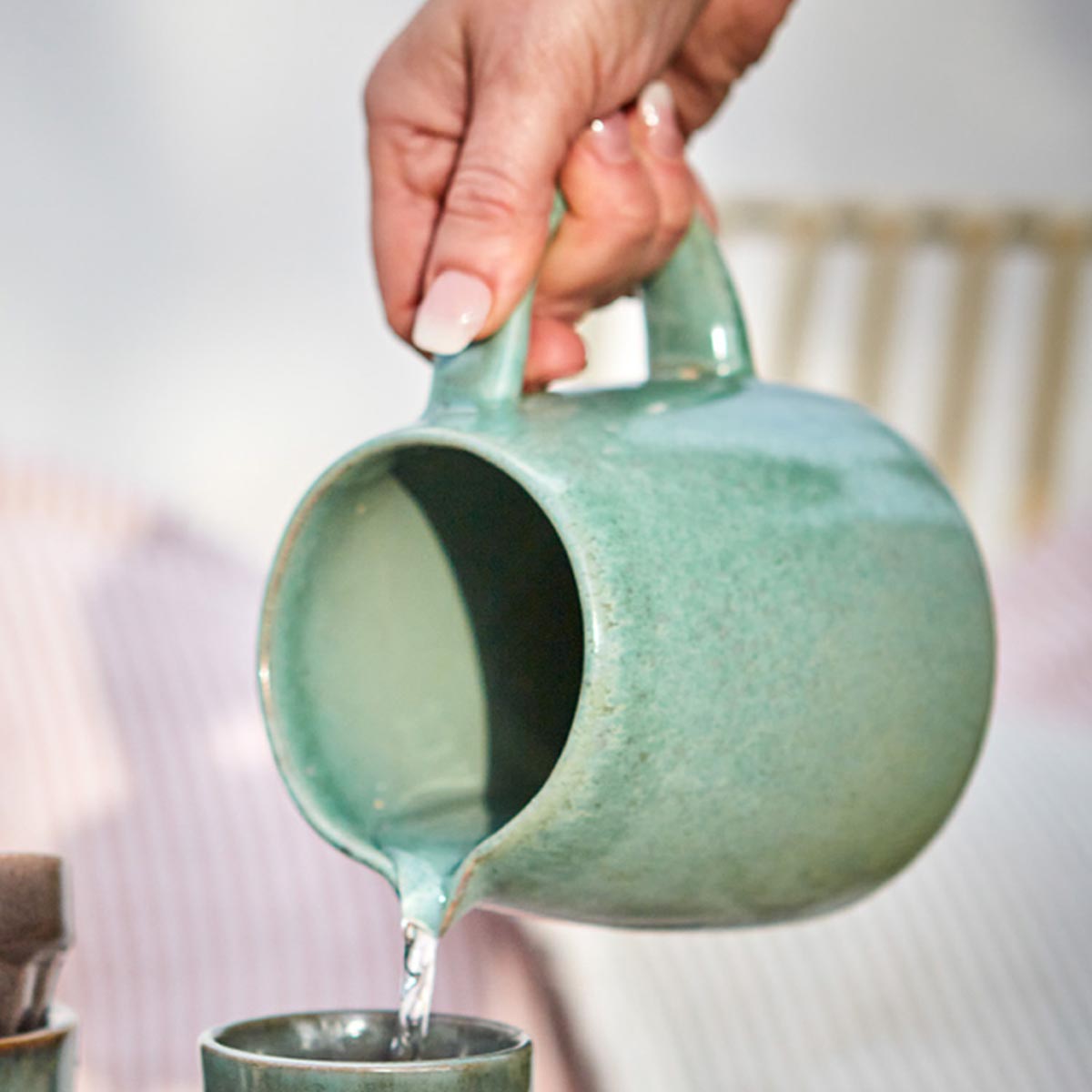 Hand pouring water from Costa Stoneware Jug in Celadon Green with natural glaze finish