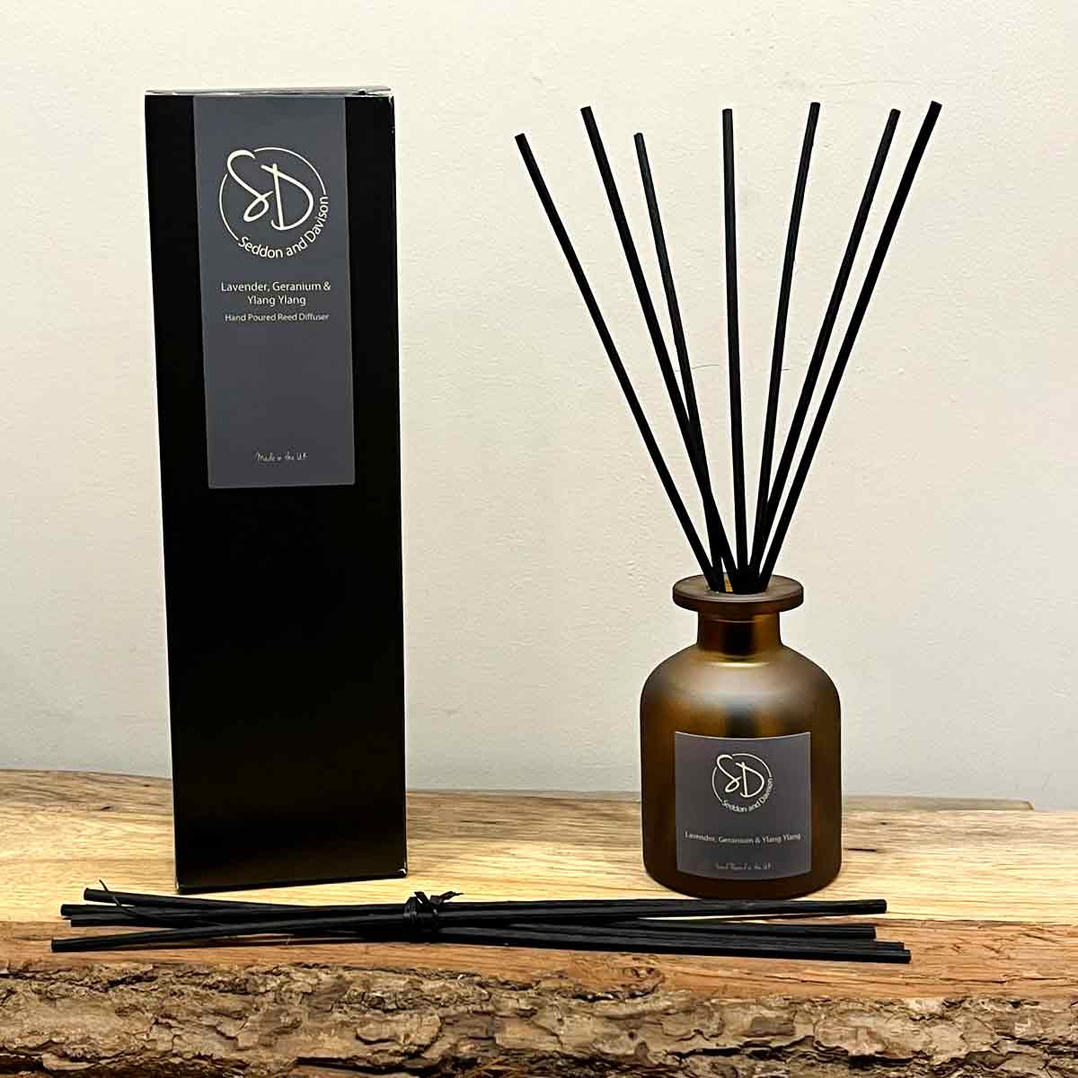 Frosted amber glass Lavender & Geranium Reed Diffuser with black reeds and packaging, set on a rustic wooden surface.