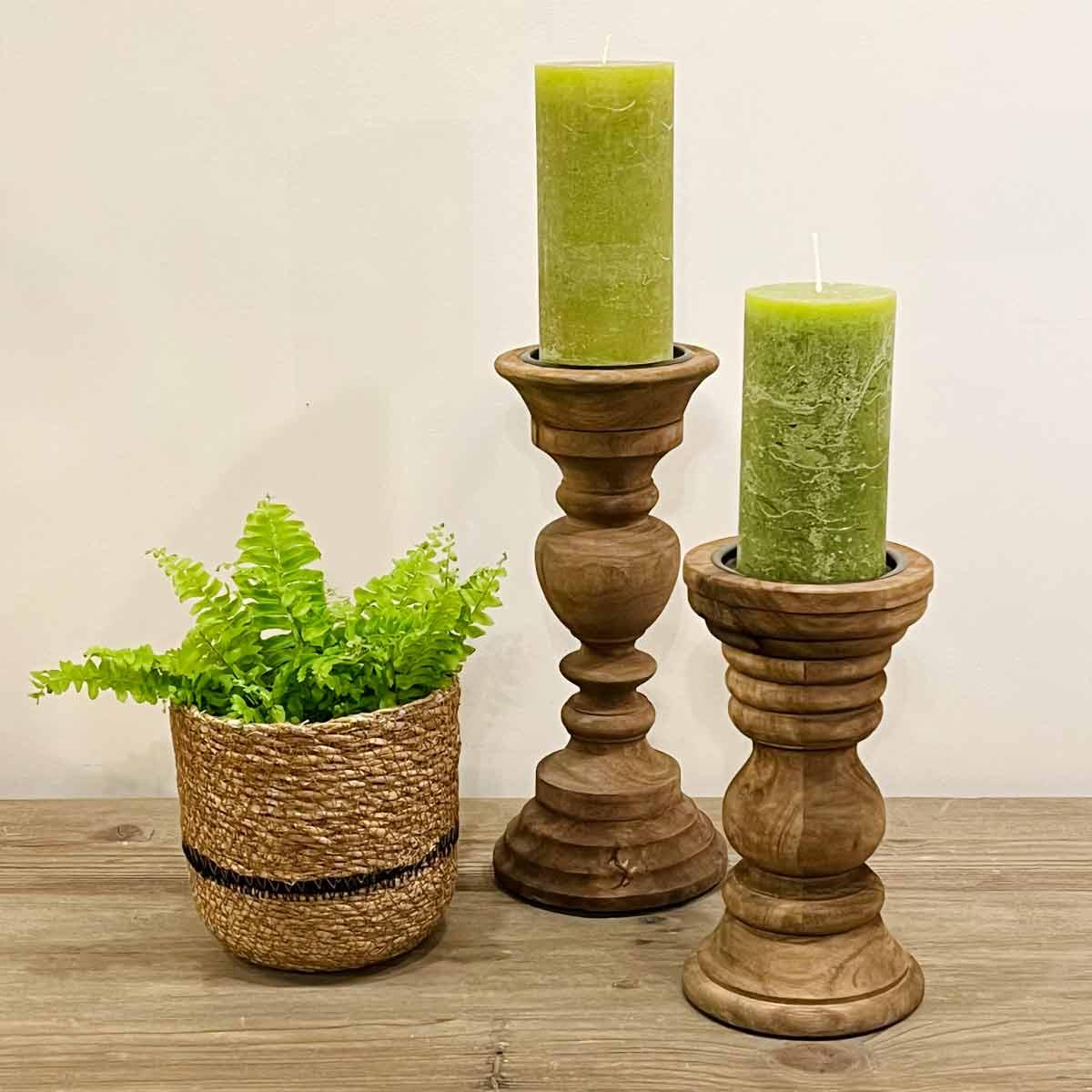 Pescara and Ravenna Mango Wood Candle Holders pictured together, styled with green pillar candles and a woven planter on a wooden surface.