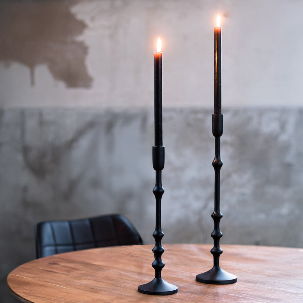 Semut Matt Black Candlesticks in two heights, displayed on a round wooden table with black tapered candles.