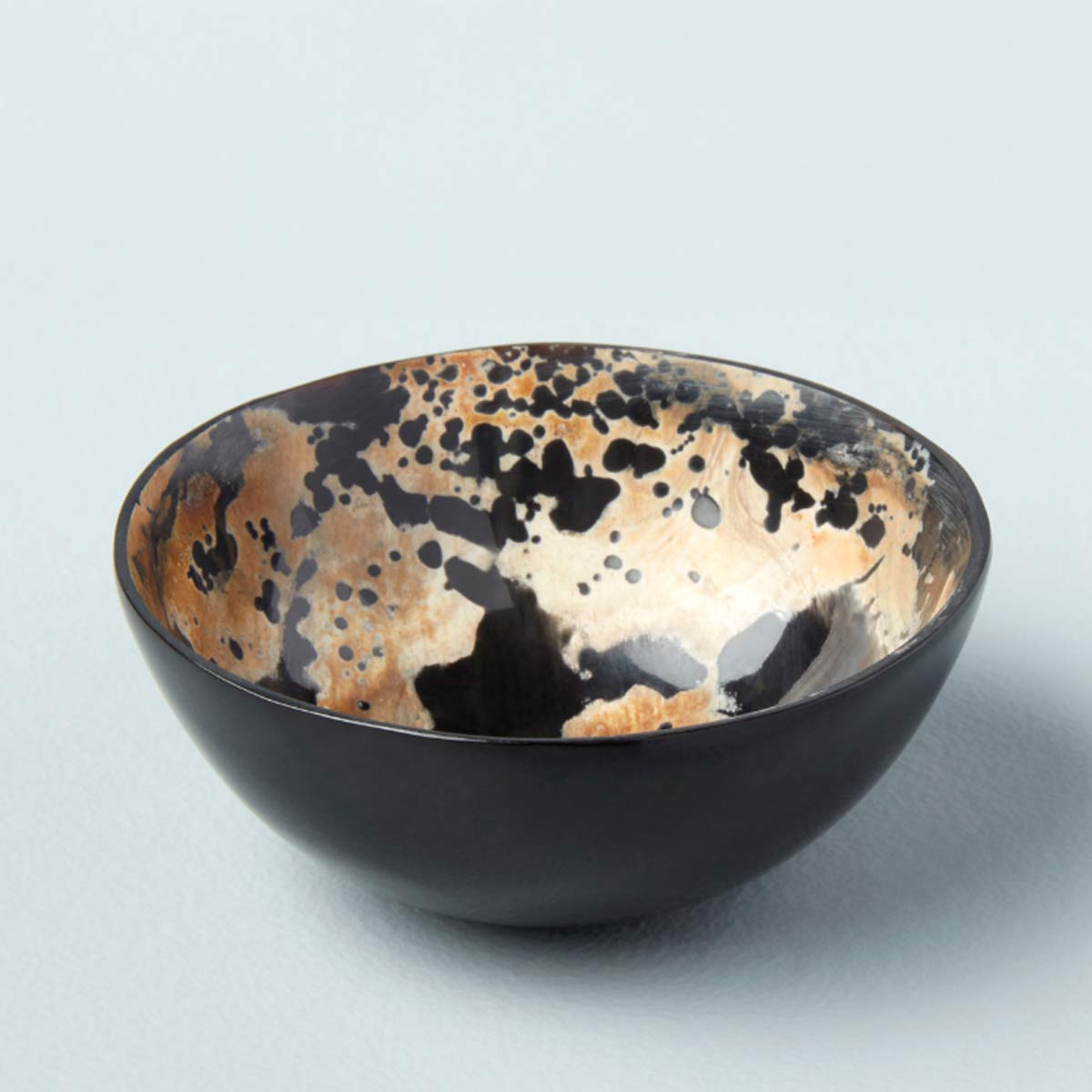 A handcrafted Splatter Horn Bowl made from ethically sourced water buffalo horn, featuring a distinctive black and caramel splatter pattern on the interior.