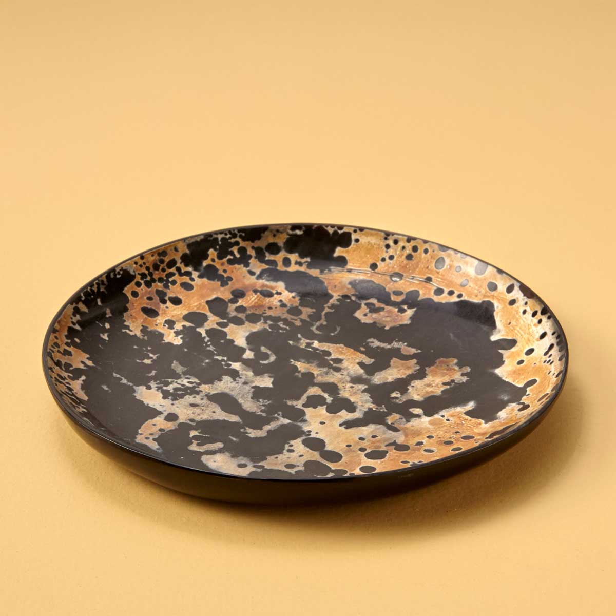 A handcrafted Splatter Horn Plate made from ethically salvaged water buffalo horn, featuring a unique hand-painted splatter design in earthy black, amber, and gold tones.