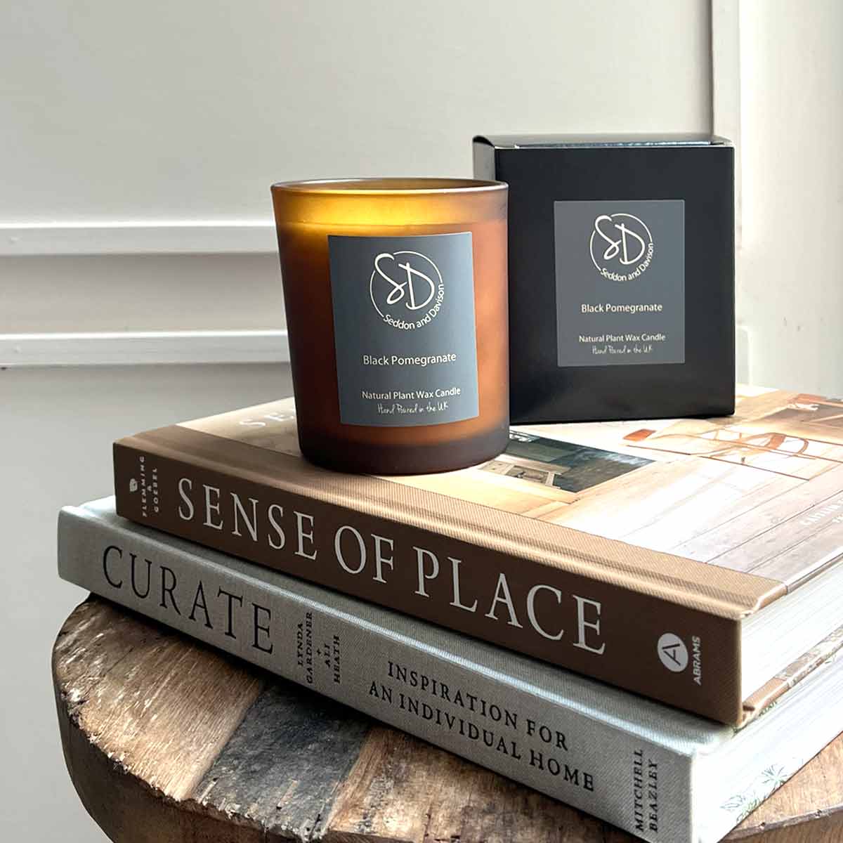 Black Pomegranate Scented Candle in a frosted amber glass jar with gift box, placed on home decor books.